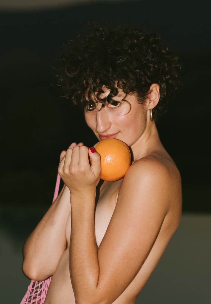 Das Foto zeigt ein junges Escortgirl mit Orange in der Hand.