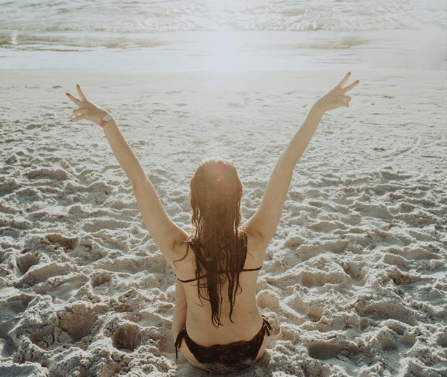 Das Foto zeigt eine Frau am Strand, die sich beim Entspannen und Träumen Ihrer sexuellen Fantasie hingibt.